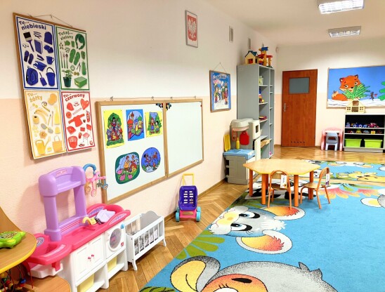 Sala przedszkolna z niebieskim dywanem i zabawkami